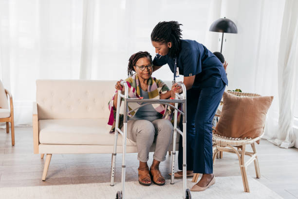 A caregiver helping a senior woman stand with a walking frame at home